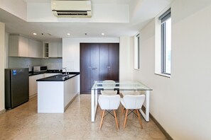 A modern kitchen with a central island, white cabinets, and a dark wood door. - Warm Space 2Br At Apartment Branz Bsd City (Tangerang)