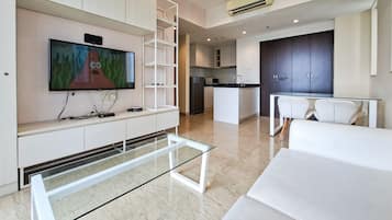 A modern living room with a flat-screen TV, a glass coffee table, and a sofa.