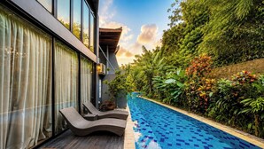 A modern outdoor pool area with a built-in seating area and lush greenery surrounding it. - Tropical Paradise 3Br At Villa Coco (Nusa Dua)