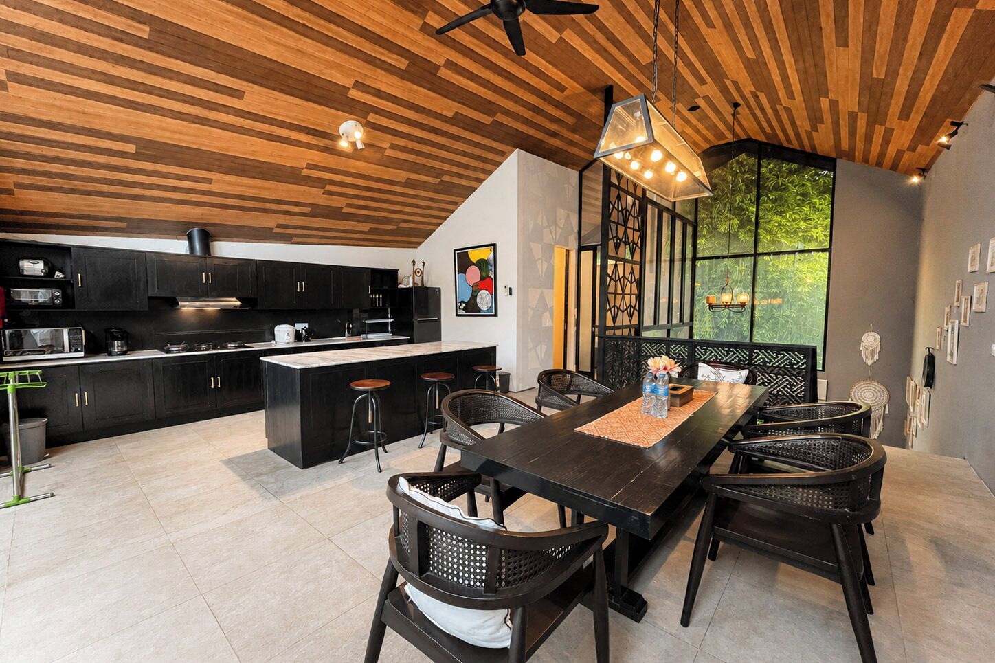 Une cuisine moderne avec des meubles de couleur sombre, un îlot central et un coin repas comprenant une longue table et des chaises.