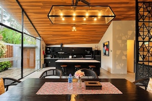 A modern kitchen with a wooden ceiling, black cabinets, and a central island with bar stools. - Tropical Paradise 3Br At Villa Coco (Nusa Dua)