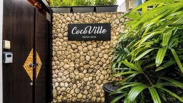 A stone wall with a sign reading 'CocoVille Nusa Dua' and a wooden door with a keyhole.