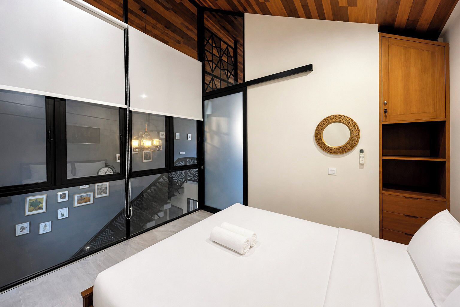 Ein modernes Schlafzimmer mit einem großen Bett, einem Holzschrank, einem an der Wand befestigten Spiegel und einer sichtbaren Treppe hinter einer Glastür.