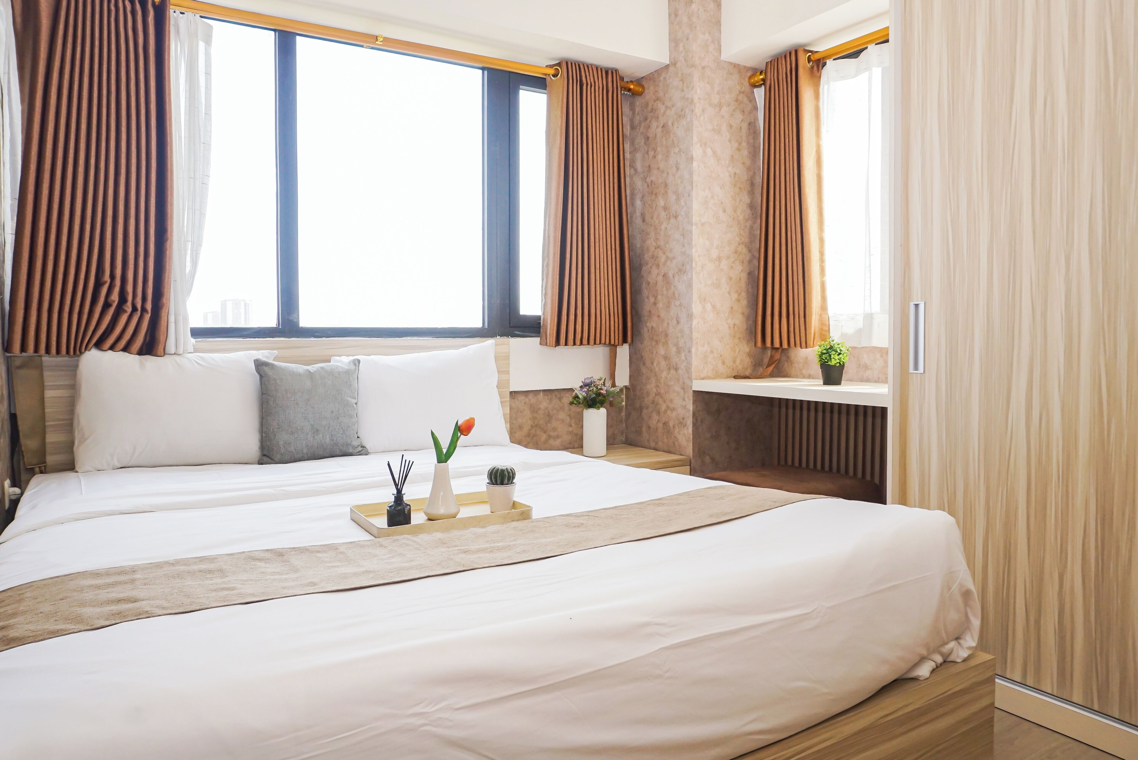 Ein Hotelzimmer mit einem großen Bett, einem Nachttisch, einer kleinen Pflanze und Blick auf die Stadt.
