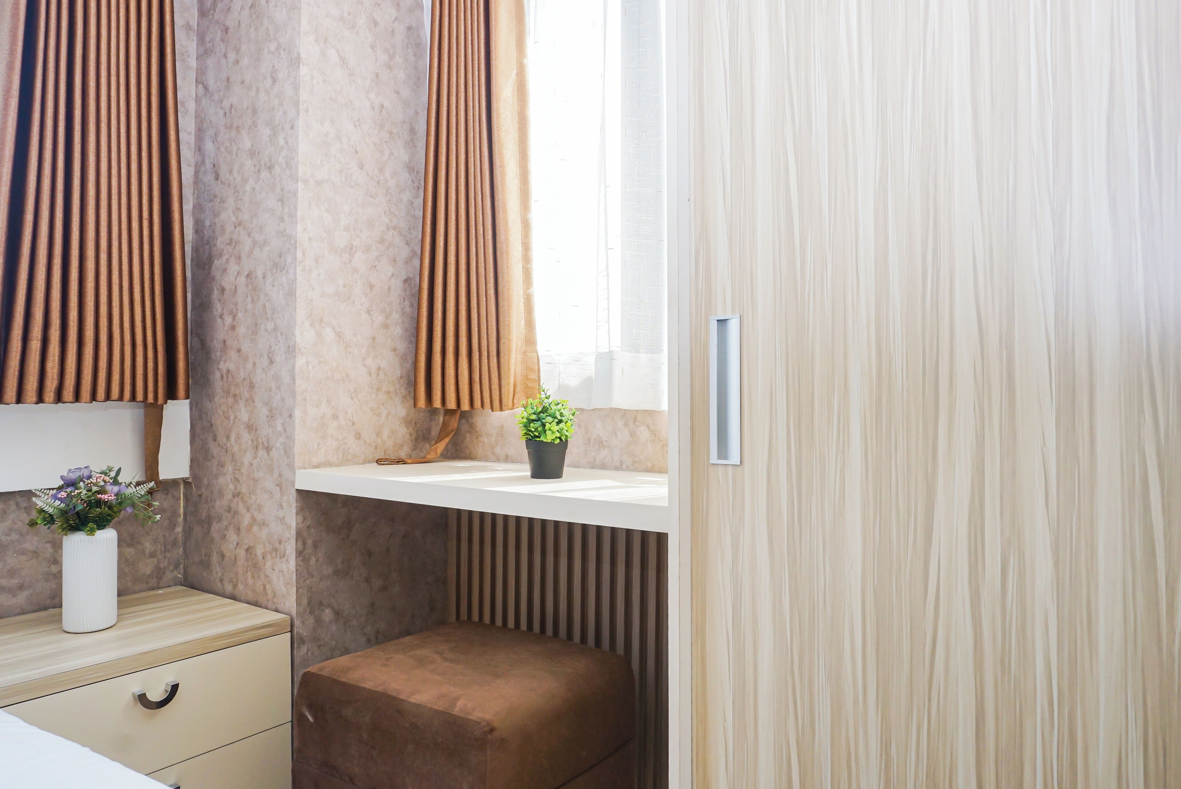 Ein Schlafzimmer mit einem Bett, einem Nachttisch, einem Fenster mit Vorhängen und einer Wandablage mit einer Pflanze.
