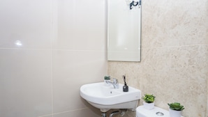 A bathroom with a white sink, a mirror, and a toilet. There are two small potted plants on the toilet. - Convenient Studio At Apartment Transpark Cibubur (Depok)