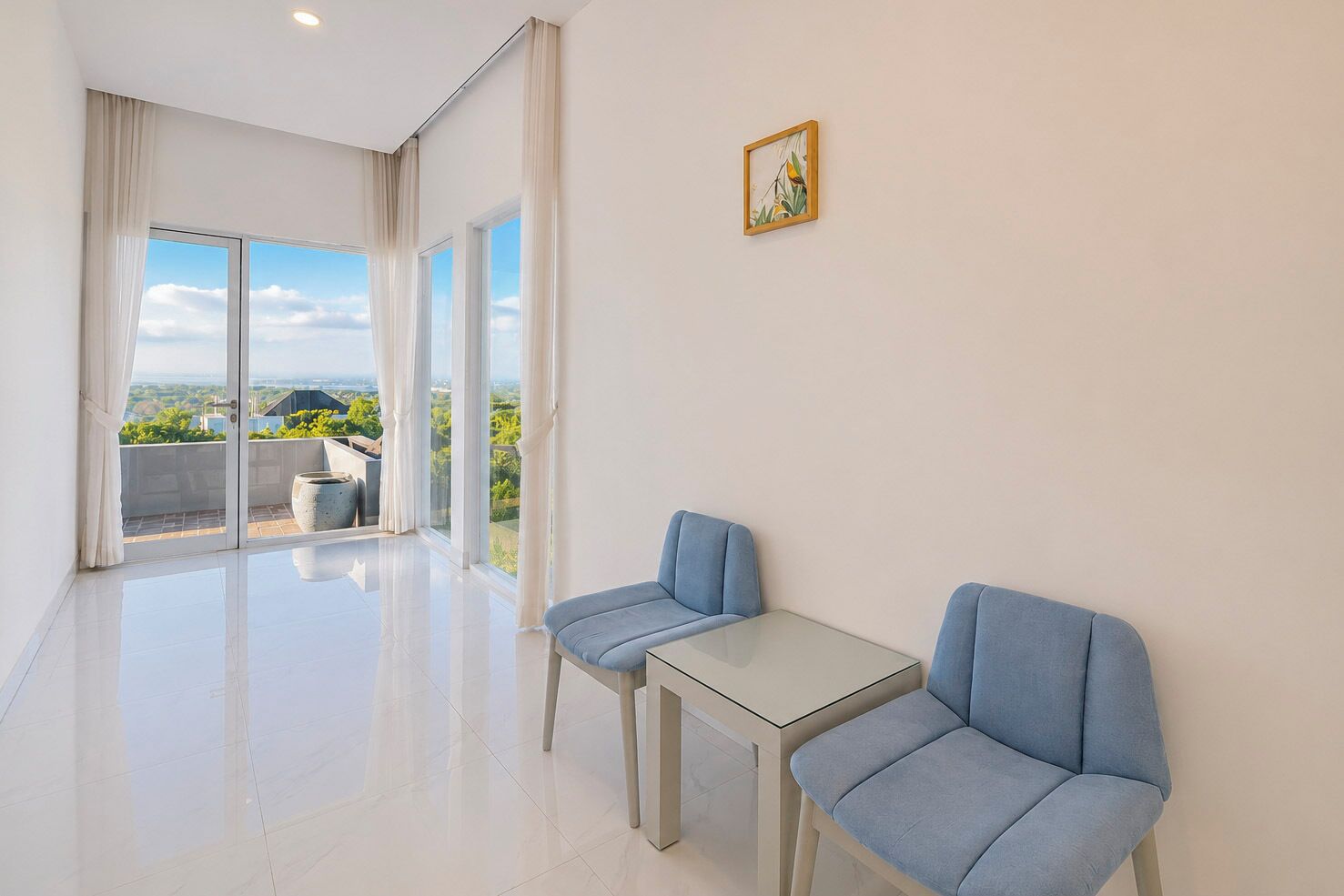 Ein modernes Zimmer mit Glastür, die auf einen Balkon führt, zwei blaue Stühle und ein kleiner Tisch.