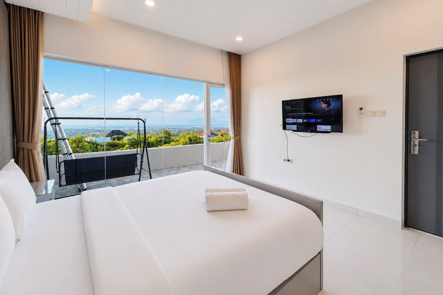 Ein Hotelzimmer mit einem großen Bett, einem an der Wand montierten Fernseher und einem Balkon mit Blick auf die Stadt.