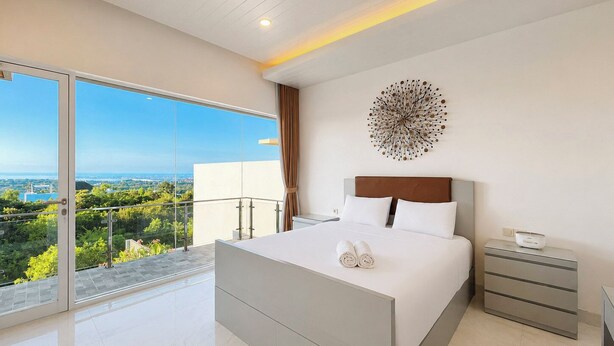 Een moderne slaapkamer met een groot bed, een nachtkastje, een decoratief object aan de muur en een balkon met uitzicht over de stad.