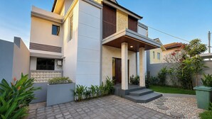 Een modern huis met twee verdiepingen, een plat dak, een balkon en een geplaveid oprit.