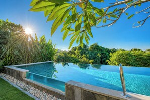 Ein klares Schwimmbecken mit Steinrand, umgeben von üppiger Vegetation und blauem Himmel.