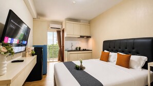 Ett hotellrum med en säng, en TV, ett skrivbord, ett litet kök och en balkong.