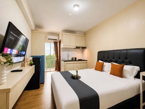 A hotel room with a bed, a TV, a desk, a kitchenette, and a balcony. - Homey Simple Studio Room At Apartment Cinere Resort (Depok)