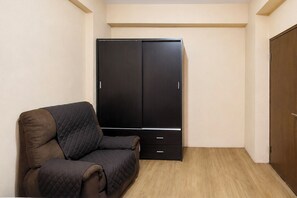 Ein kleines Zimmer mit einem Einzelbett, einem Kleiderschrank und einer Tür.