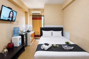 A hotel room with a bed, a television, a water dispenser, a kettle, and a small table with a remote control and flowers. - Classic Homey Studio Room At Apartment Gateway Ahmad Yani Cicadas (Bandung)
