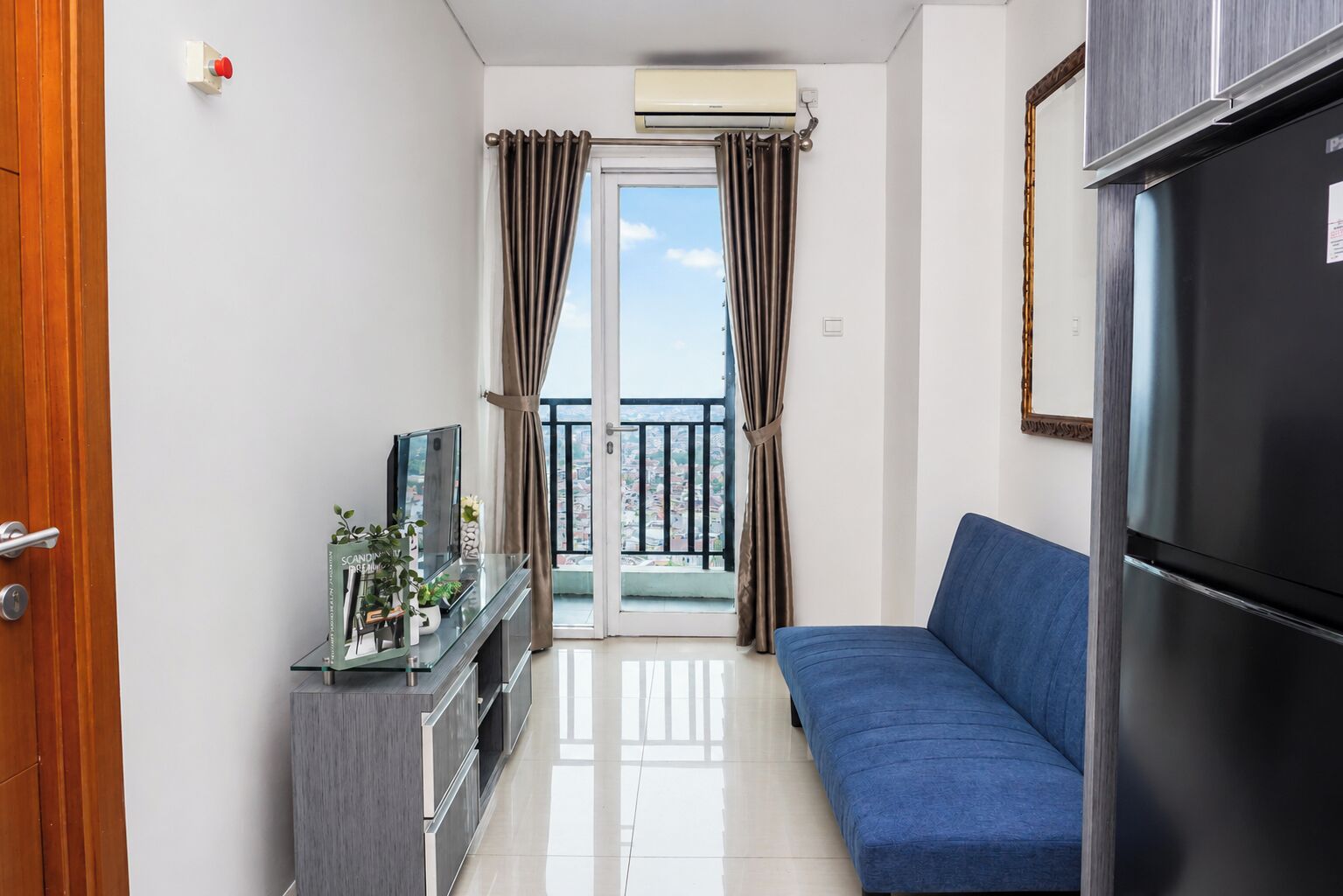 A modern apartment with a balcony, a sofa, a TV, and a refrigerator.