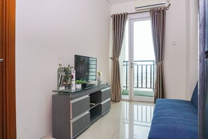 A modern living room with a flat-screen TV, a glass coffee table, and a blue sofa. - Best Deal And Modern 1Br Woodland Park Residence (Jakarta)