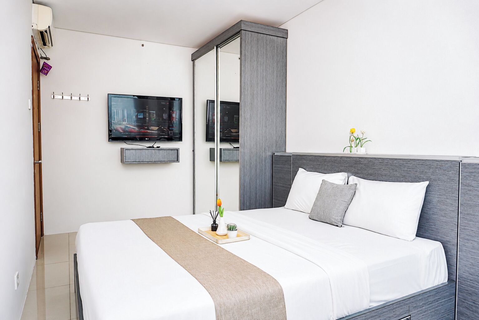 A modern hotel room with a large bed, a flat-screen TV mounted on the wall, and a small table with decorative items.