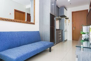 Ein modernes Wohnzimmer mit einem blauen Sofa, einem Glastisch und einer Küchenzeile mit Schränken und einem Kühlschrank.