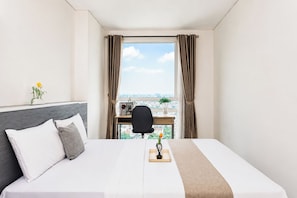 Ein Hotelzimmer mit Bett, Schreibtisch, Stuhl, einem Fenster mit Vorhängen und Blick auf die Stadt.
