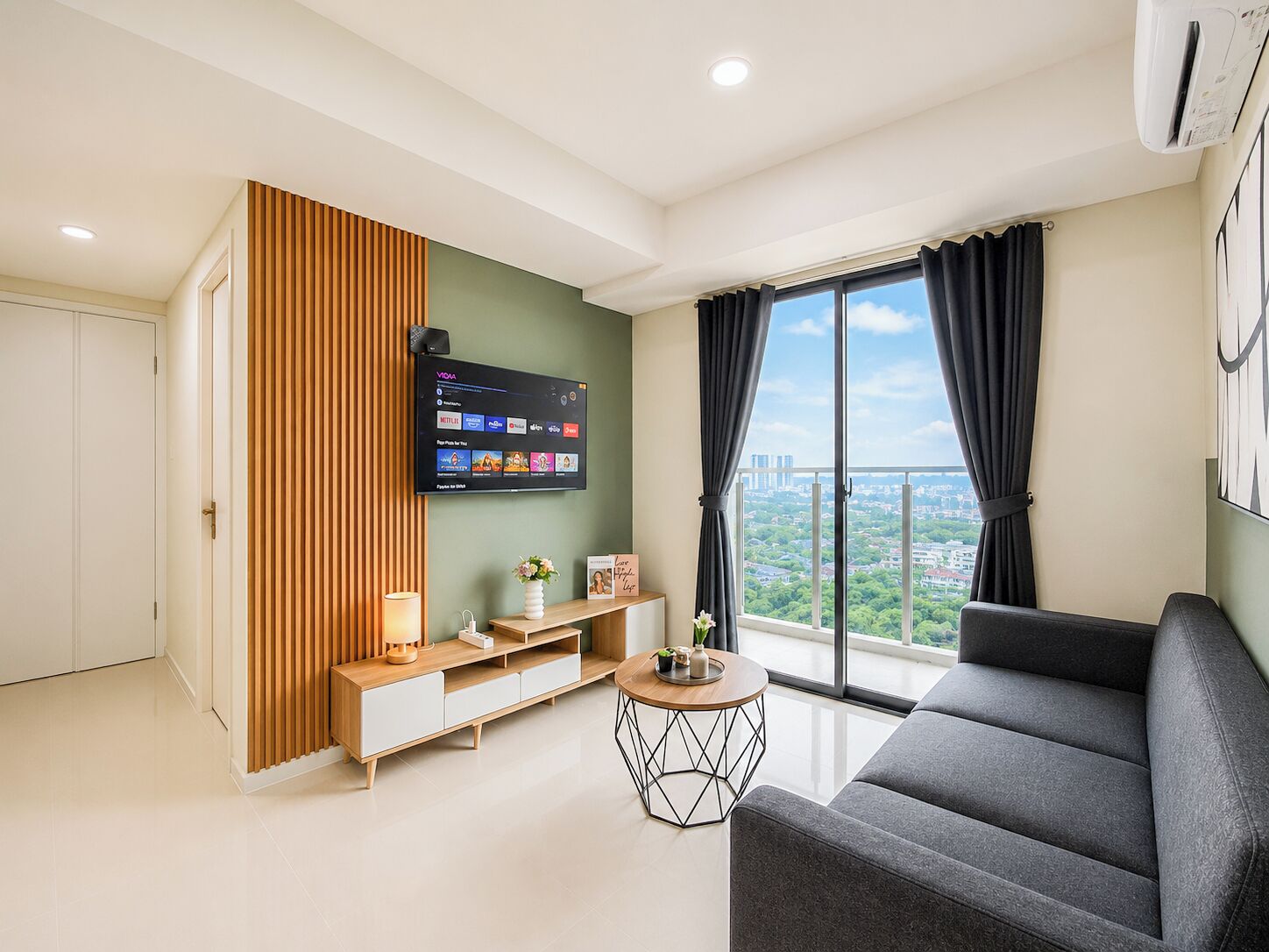 A modern living room with a flat-screen TV, a sofa, a coffee table, and a view of the city through large windows.