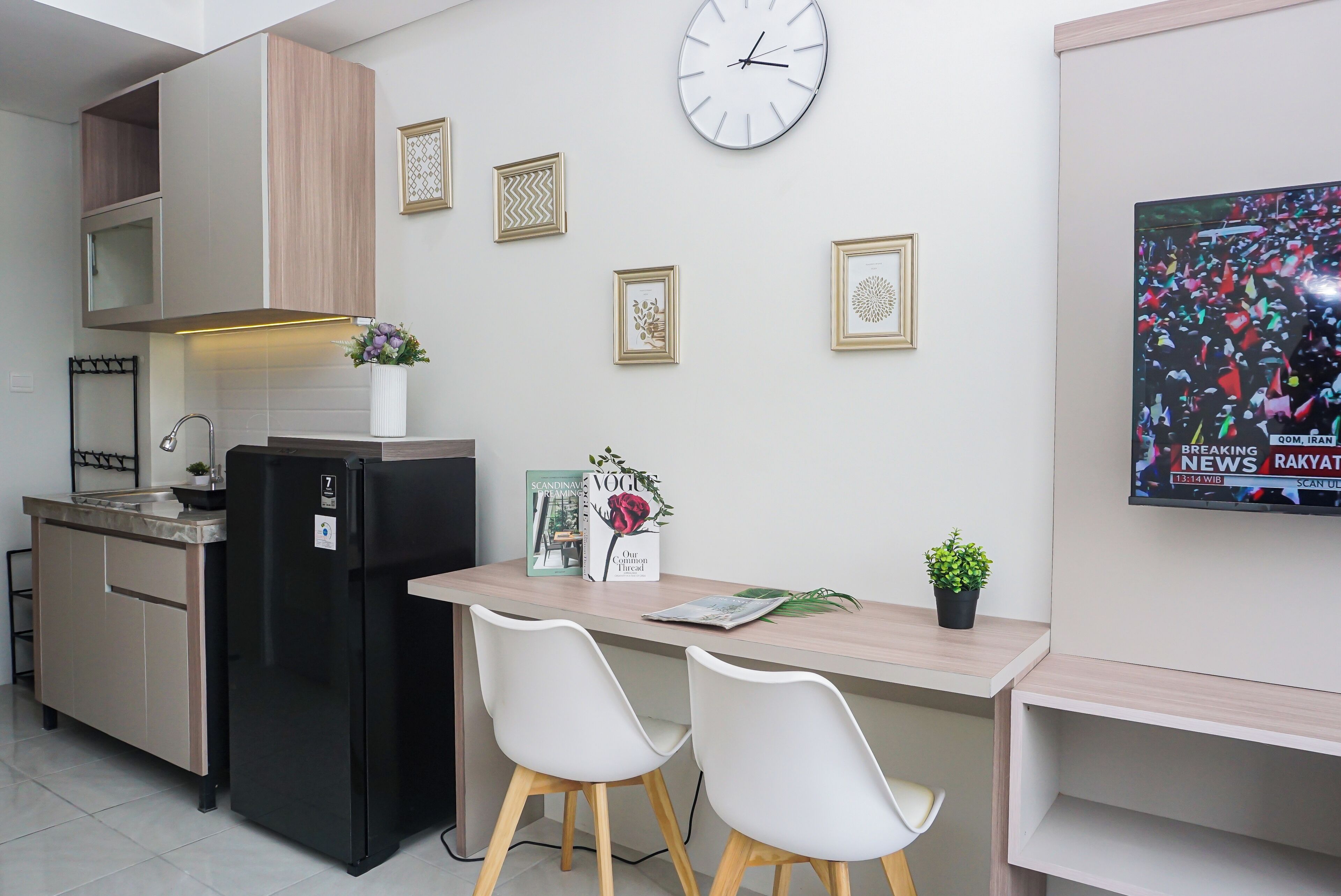 A modern kitchen with a refrigerator, a microwave, and a sink. There are two white chairs and a small table with a potted plant.