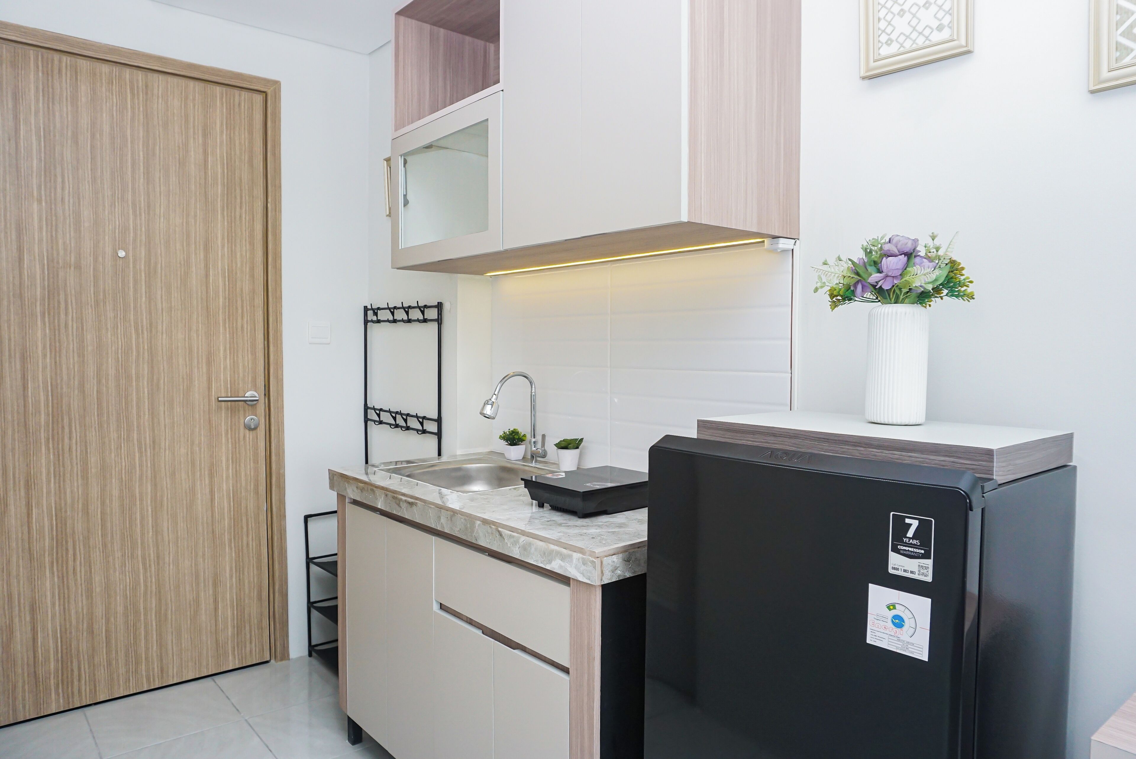 Una cocina compacta con un lavamanos integrado, un refrigerador negro y una puerta de madera.