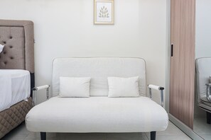 Ein modernes Schlafzimmer mit einem weißen Polsterstuhl, einem Bett mit einer gesteppten Kopfteil sowie einem gerahmten Kunstwerk an der Wand.