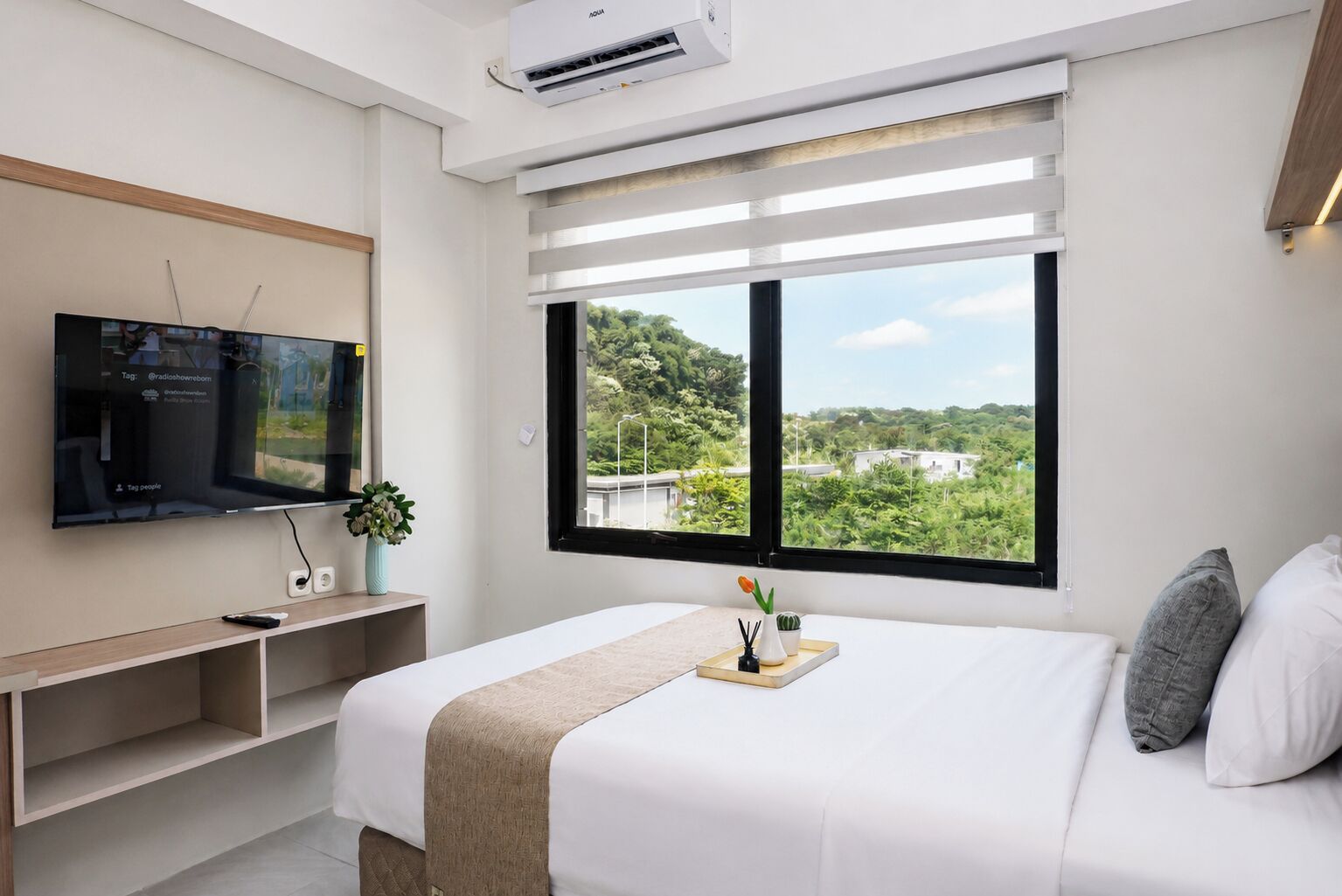 Quarto de hotel moderno com cama, televisão, janela com vista e ar condicionado integrado.