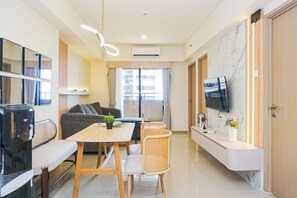 A modern living room with a sofa, a dining table, and a TV mounted on the wall. - Cozy And Functional 3Br At Apartment Meikarta (Cikarang)