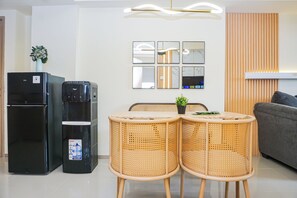 Un espacio habitable moderno con un refrigerador negro, una cafetera, una mesa de comedor con dos sillas y un sofá gris.
