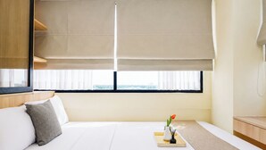 Een hotelkamer met een bed, nachtkastje, raam met zonwering en uitzicht op het landschap.