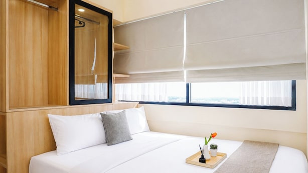 Een hotelkamer met een bed, een houten kast, een raam met zonwering en een dienblad met een vaas en bloemen.