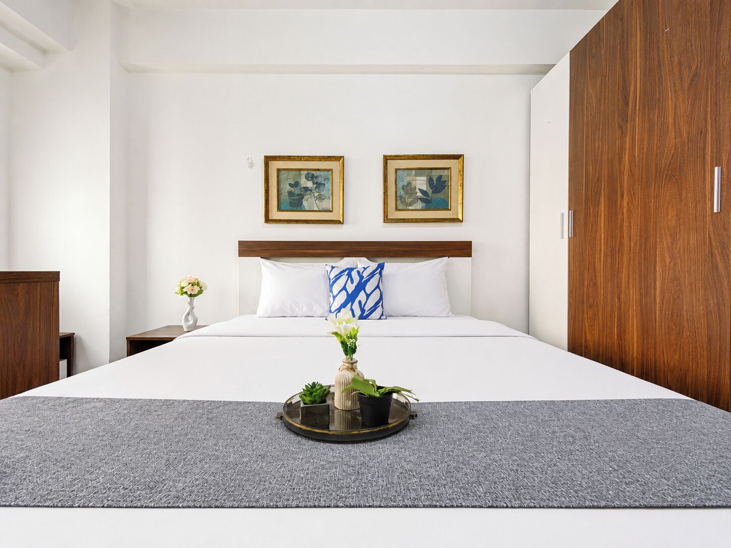 Une chambre d’hôtel avec un lit, une table de chevet, une commode et deux tableaux encadrés au mur.
