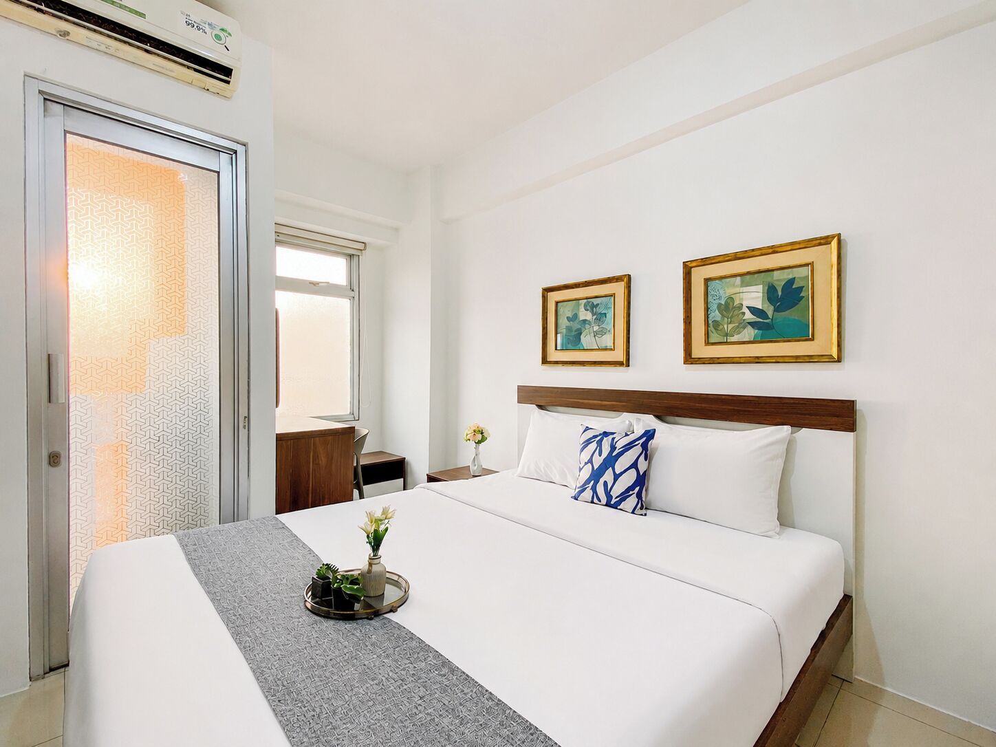 Une chambre d’hôtel avec un lit, un bureau, une chaise, une fenêtre et deux tableaux encadrés au mur.