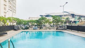 An outdoor swimming pool with a metal railing, surrounded by trees and a fence. - Minimalist And Homey Studio At Apartment Tifolia (Jakarta)