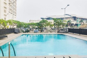 Piscina ao ar livre com grade de metal, cercada por árvores e um muro.