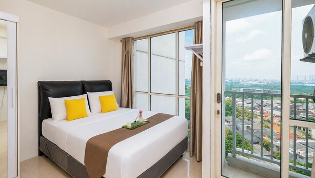 A hotel room with a bed, a view of the city through large windows, and a balcony with a railing. - Minimalist And Homey Studio At Apartment Tifolia (Jakarta)
