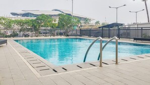 A swimming pool with a metal ladder, surrounded by a tiled deck and a fence. - Minimalist And Homey Studio At Apartment Tifolia (Jakarta)