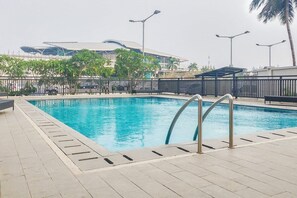 Piscina com escada de metal, cercada por um deck revestido com azulejos e uma grade.