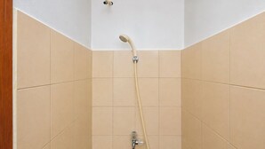 A shower with a handheld showerhead and a wall-mounted faucet in a corner of a room with beige tiled walls. - Minimalist And Homey Studio At Apartment Tifolia (Jakarta)
