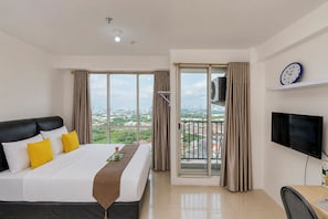 A hotel room with a bed, a TV, a desk, and a balcony with a city view.