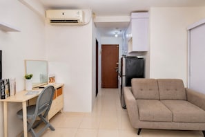 A compact living space with a kitchenette, a sofa, a desk with a chair, and a mirror.