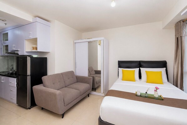 A hotel room with a bed, a sofa, a kitchenette, and a bathroom.