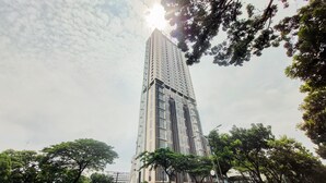 A tall, modern building with a glass facade, surrounded by trees and parked cars. - Refined 2Br At Apartment Transpark Bintaro (Tangerang)