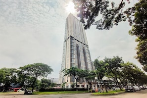 A tall, modern building with a glass facade, surrounded by trees and parked cars. - Refined 2Br At Apartment Transpark Bintaro (Tangerang)