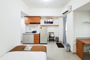 A compact hotel room with a kitchenette, a bed, a TV, and a small bathroom. - Functional Simple Studio Room At Apartment Cisauk Point (Cisauk)