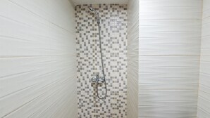Eine Dusche mit gefliesten Wänden und einem Metall-Duschkopf.