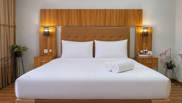A neatly made bed with white linens, a wooden headboard, and two bedside tables with lamps. - Modern Breezy Studio At Apartment Tamansari Skylounge Balikpapan (Balikpapan)