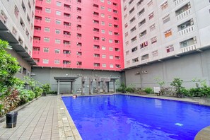 Edifício residencial com piscina, rodeado por vegetação e uma entrada coberta.